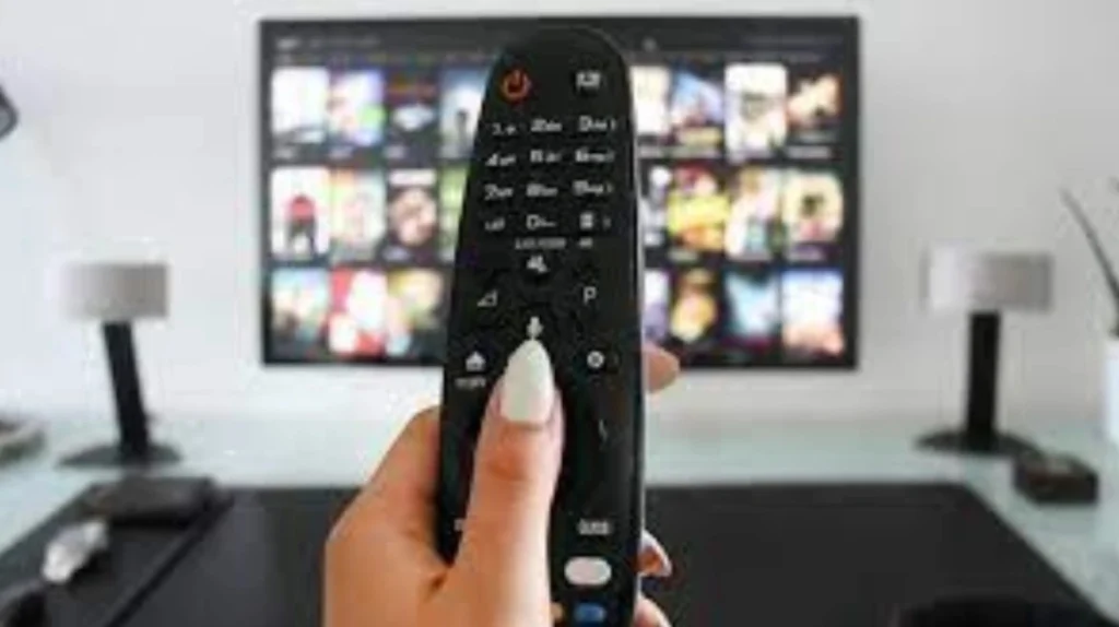 Close-up of a hand holding a remote control pointed at a TV screen displaying IPTV Germany interface with various movie and TV show thumbnails—demonstrating user-friendly navigation and content access.